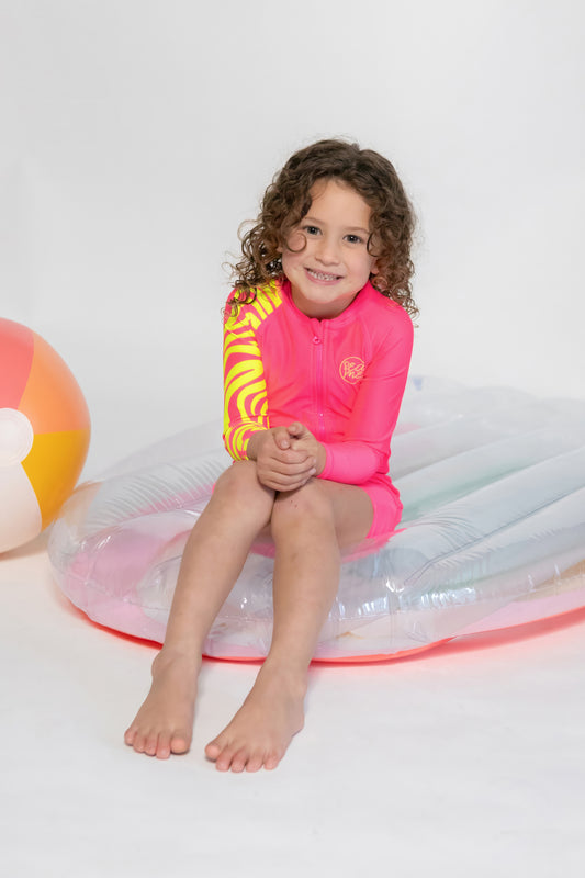 A toddler in a bright pink long sleeve swimsuit with a unique one-armed zebra print sleeve, sitting on a inflatable ring.